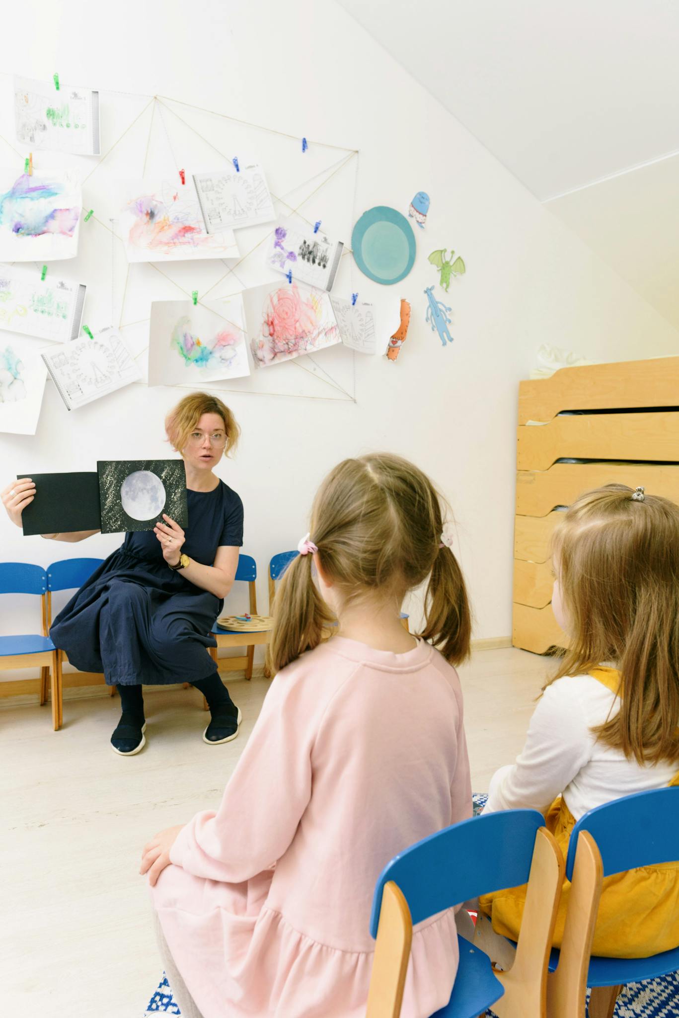 A teacher shows a book to children in a creative kindergarten setting.